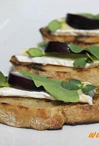 Three toasted crostini slices topped with soft cheese, a beet round, and fresh greens on a white surface.