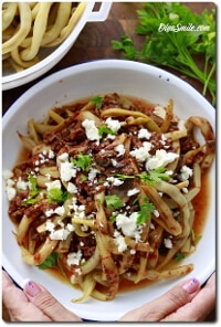 Pasta in tomato sauce with crumbled feta and parsley, served in a white bowl and held by two hands.