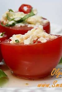 Two red bell peppers filled with a creamy cheese filling, garnished with herbs on a white plate.