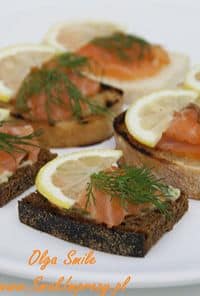 Open-faced rye toasts topped with smoked salmon, lemon slices, and fresh dill on a white plate.