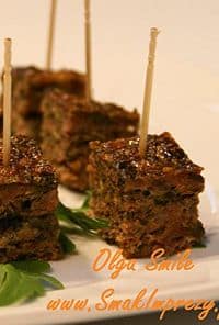 Three chocolate brownie bites on a white plate, each with a wooden toothpick and a small green garnish nearby.