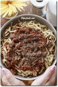 Hands hold a bowl of spaghetti with meat sauce in a cozy kitchen.