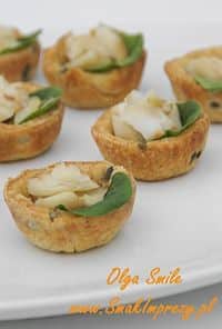 Five bite-sized savory tartlets with greens and melted cheese arranged on a white plate.