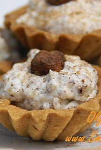 Close-up of mini tart shells filled with creamy vanilla icing, dusted with cocoa and topped with a hazelnut.