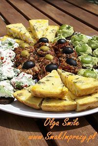Assorted cheese wedges, olives, nuts, and fruit arranged on a round platter on a wooden table.