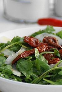 Salad bowl with arugula, shaved parmesan, and sun-dried tomatoes on top of a light dressing
