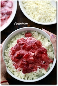 Bowl of cauliflower rice topped with strawberry sauce, held by hands with other bowls in the background.
