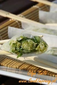 Dumpling with a green vegetable filling held by chopsticks above a plate of dumplings, ready to eat.