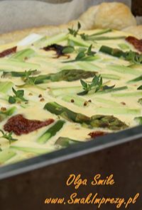 Baked zucchini gratin with melted cheese, dollops of pesto, sun-dried tomatoes, and fresh herbs in a baking pan.